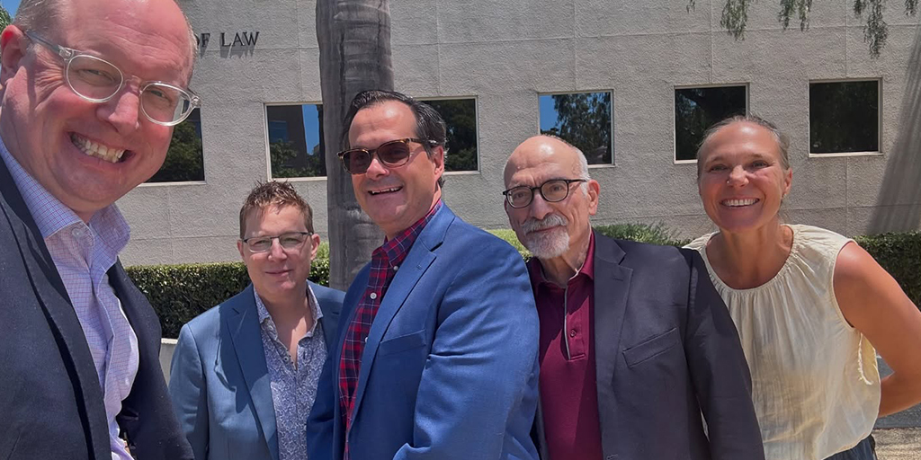 An outdoor photo of five smiling people in businesswear