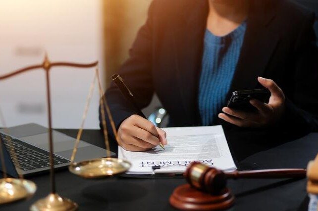 Woman lawyer at desk signing a paper with scales of justice nearby